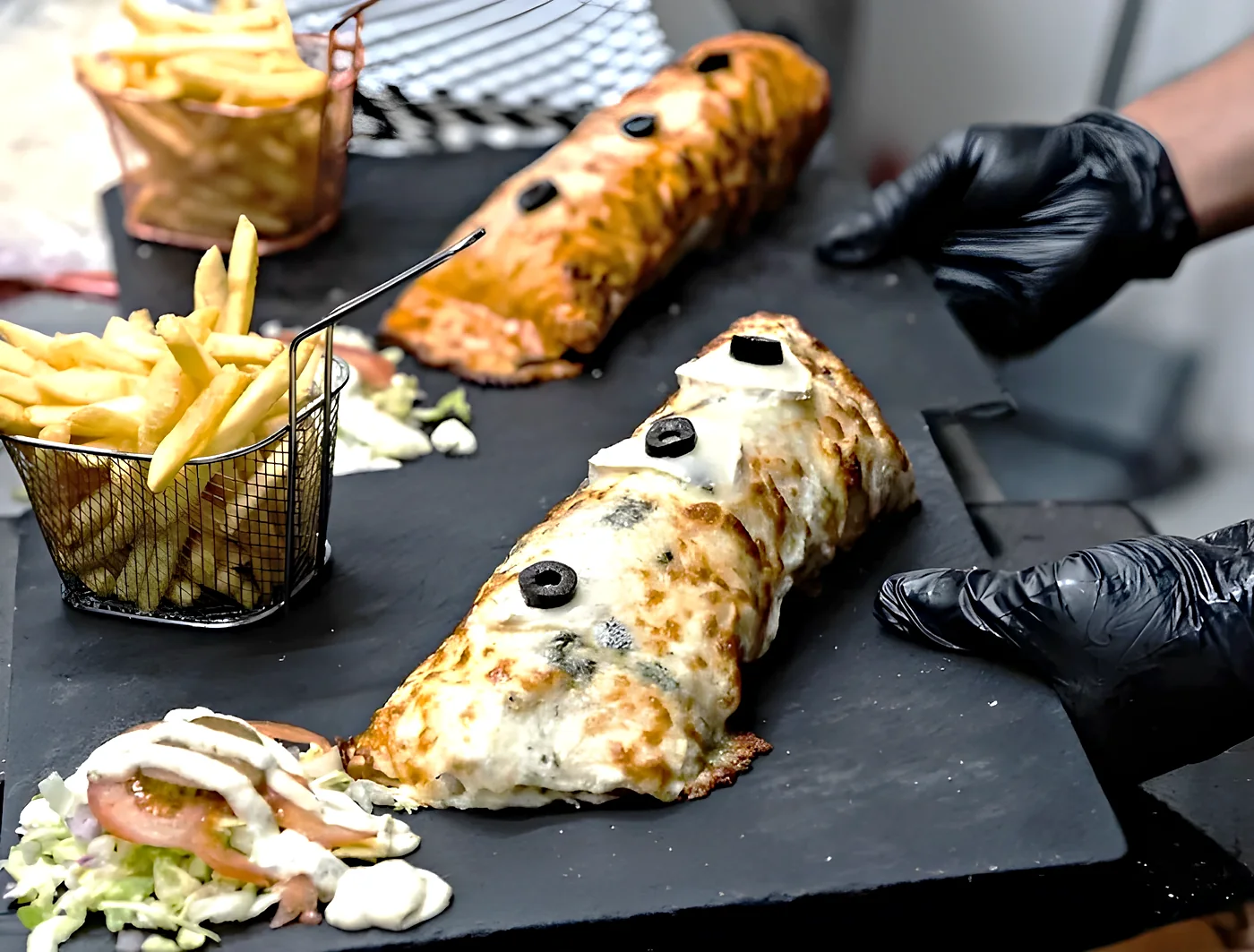 Deux tacos Signature gratinés aux olives sur ardoise, avec frites maison et salade