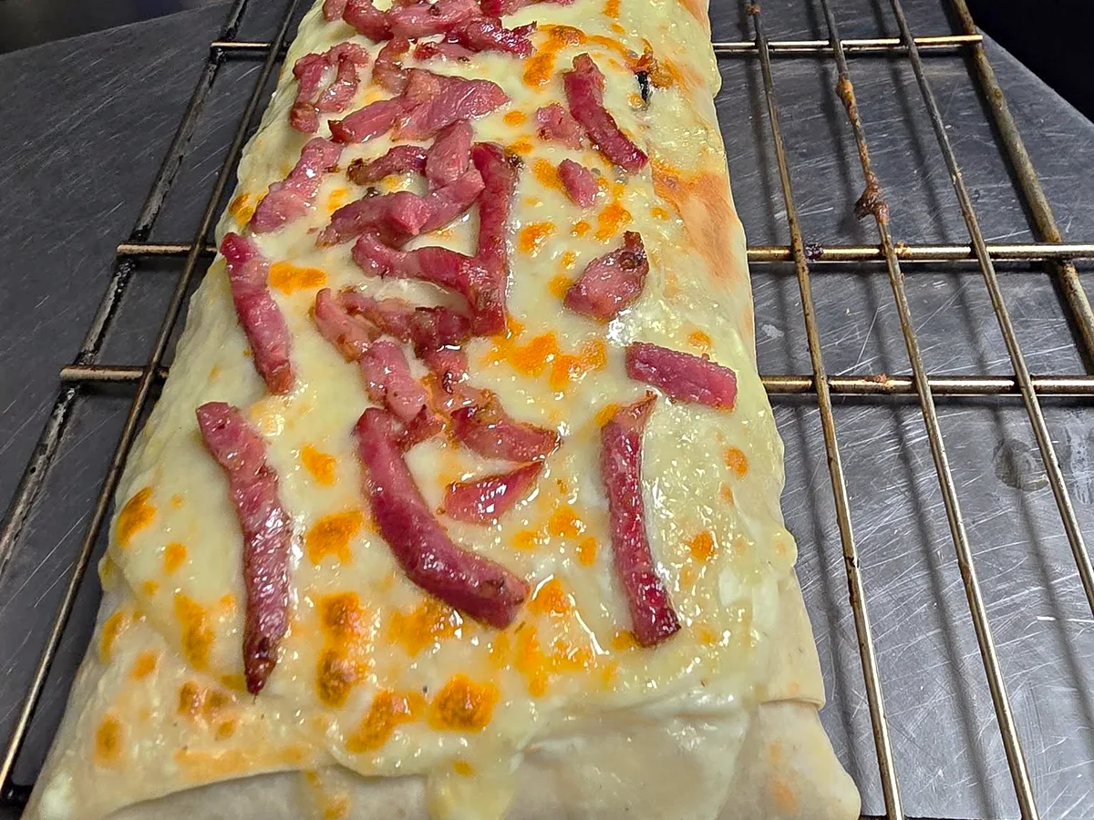 Tacos gratiné à la raclette, couvert de lardons grillés, à la sortie du four